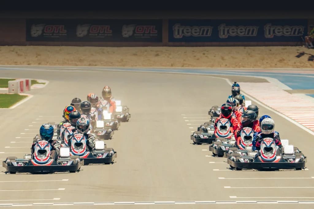 Two columns of rental karts rolling toward the start on an outdoor circuit in daylight
